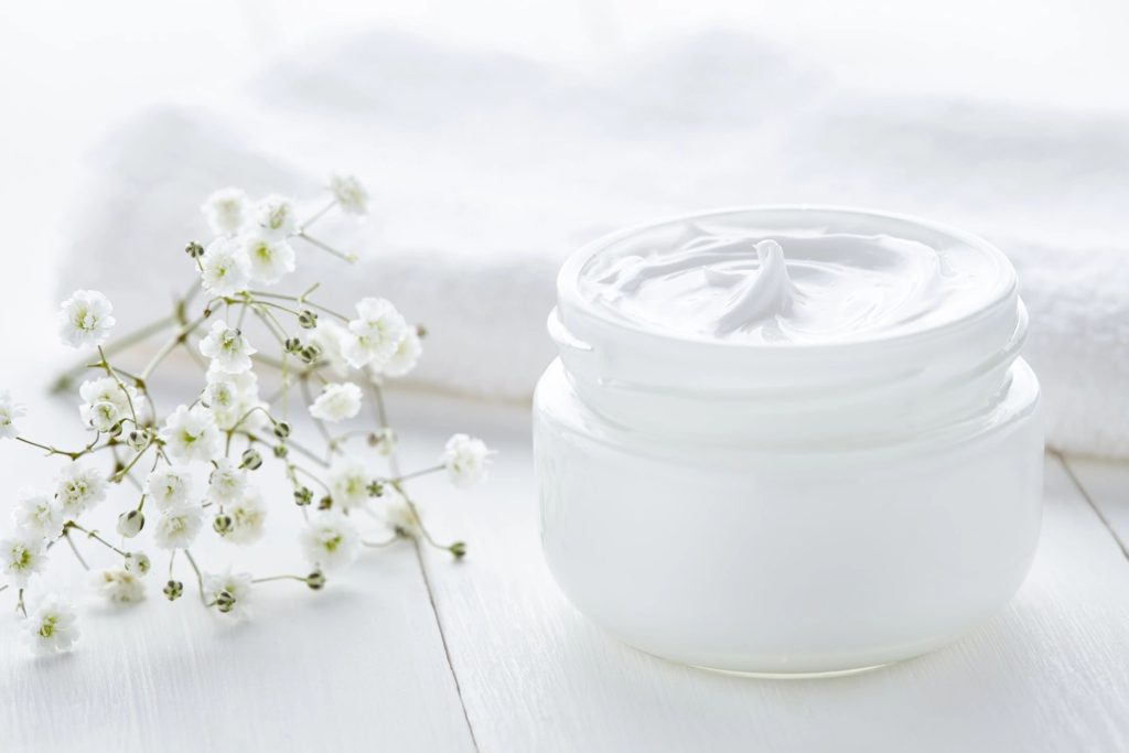 A jar of cream sitting next to some flowers.