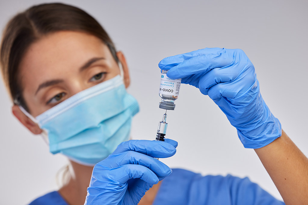 A woman in blue gloves holding up an injection.